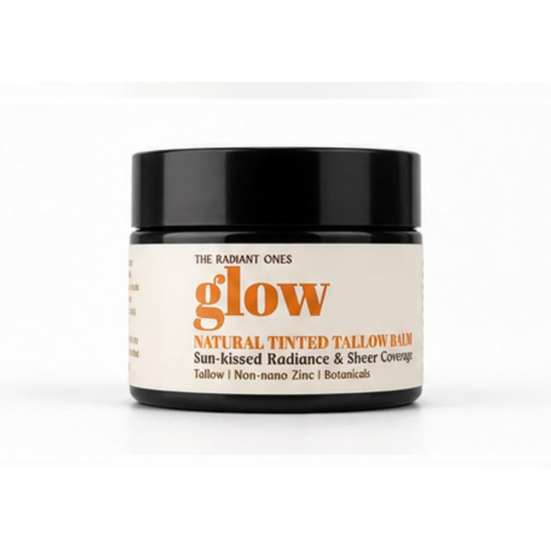 May include: A black cylindrical jar of The Radiant Ones Glow natural tinted tallow balm. The cream-colored label features orange text reading glow, with additional text: Natural Tinted Tallow Balm, Sun-kissed Radiance & Sheer Coverage, Tallow, Non-nano Zinc, Botanicals.