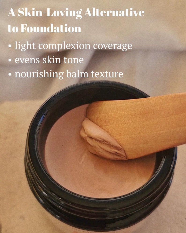 May include: A black jar containing a beige-toned cosmetic balm with a wooden spatula scooping a portion. Text reads: A Skin-Loving Alternative to Foundation, light complexion coverage, evens skin tone, nourishing balm texture.