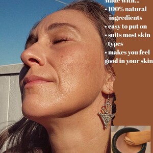 May include: A small black jar containing a light-toned cosmetic cream with a wooden applicator. The image includes text: Made with... 100% natural ingredients, easy to put on, suits most skin types, makes you feel good in your skin.