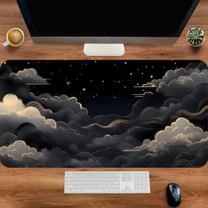 May include: A black and gold desk mat featuring a cloud and starry night design. The mat has a rectangular shape and is placed on a wooden desk. A white keyboard and black mouse are visible.
