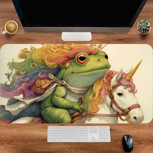 May include: A whimsical mouse pad featuring a green frog riding a white unicorn. The frog has rainbow-colored hair and is wearing a cape. The unicorn has a golden horn and a pink mane. The background is a light beige color.