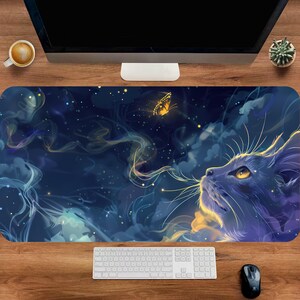 May include: A large, rectangular desk mat featuring a digital art design. The artwork depicts a dark blue cat gazing upwards at a yellow butterfly against a backdrop of swirling clouds and stars. The mat is placed on a wooden desk.