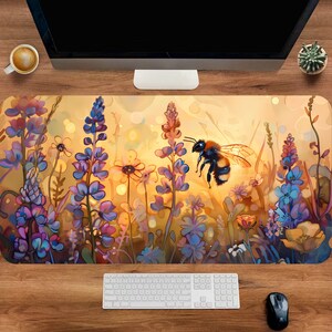 Op de afbeelding: Een rechthoekige bureaumat met een levendige illustratie van een hommel die boven een veld met wilde bloemen zweeft. Het kunstwerk toont een warm kleurenpalet met tinten geel, paars en blauw, waardoor een zonnige, natuurlijke scène ontstaat.