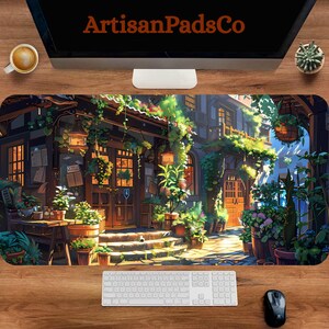 May include: A large rectangular desk mat featuring a detailed illustration of a European street scene with shops, plants, and hanging lanterns. The mat has the text "ArtisanPadsCo" at the top. A keyboard, mouse, and monitor are visible.