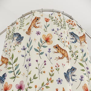 May include: A white shower curtain with a repeating pattern of frogs and flowers. The frogs are in shades of blue, orange, and brown. The flowers are in shades of pink, orange, and yellow.