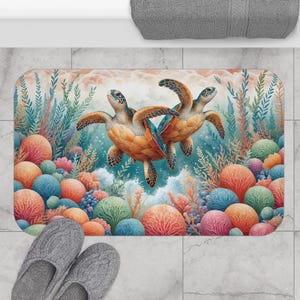 May include: A bath mat with a colorful coral reef design featuring three sea turtles swimming in the ocean. The mat has a light blue background with pink, orange, and green coral.