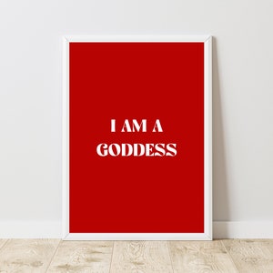 Könnte beinhalten: Ein weißer gerahmter Druck mit rotem Hintergrund und dem Text "I AM A GODDESS" in Weiß.