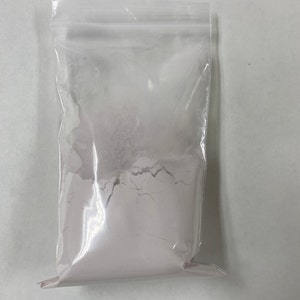 May include: A clear plastic bag filled with a light purple powder.