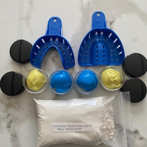 May include: Dental impression kit featuring two blue trays, black containers, clear containers with yellow and blue materials, and a bag of white powder. The bag has text that reads "Dental Stone/ Plaster Powder 150 Gr Mixer 100 Gm/ 30 Ml."
