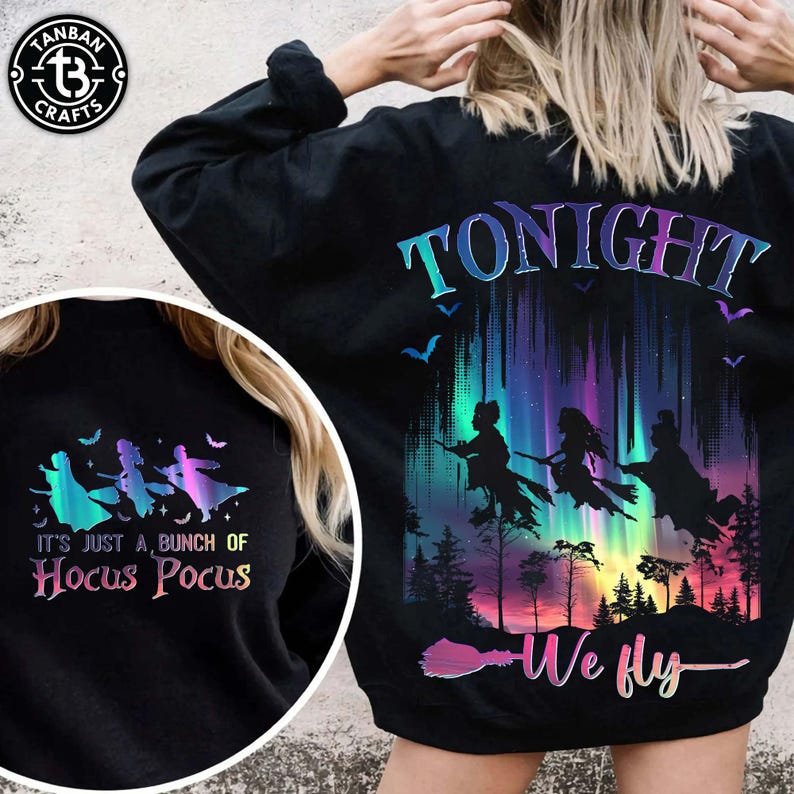 Puede incluir: Sudadera negra con un gr&aacute;fico colorido que muestra siluetas de brujas volando por un cielo nocturno con el texto "Tonight We Fly". La parte delantera de la sudadera tiene el texto "It's Just a Bunch of Hocus Pocus".