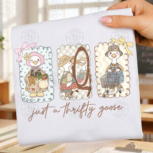 Puede incluir: Una camiseta blanca con tres ilustraciones enmarcadas de un ganso de dibujos animados. El ganso se muestra con diferentes atuendos, incluyendo un gorro, un vestido y un peto, con el texto "just a thrifty goose" debajo.