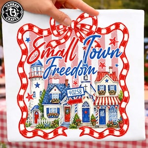 May include: A square canvas print with a patriotic design. It features the words "Small Town Freedom" in red and blue script. The image shows a quaint town scene with a lighthouse, houses, and a church, framed by a red and white ribbon.