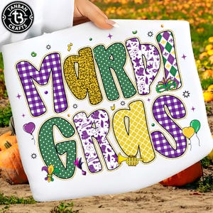 May include: White fabric with the words "MARDI GRAS" in large, colorful letters. The letters are decorated with various patterns, including purple gingham, leopard print, polka dots, and fleur-de-lis. The design includes stars, balloons, and a trumpet.