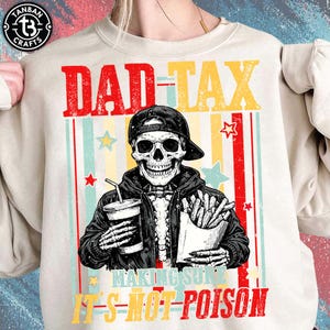 May include: Beige sweatshirt with a graphic of a skeleton wearing a cap and jacket, holding a drink and fries. Text reads "DAD TAX" and "MAKING SURE IT'S NOT POISON" in red, yellow, and blue.