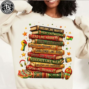 May include: White sweatshirt featuring a stack of books with inspirational quotes like "Dream Like Martin" and "Lead Like Harriet." The design includes stars, a raised fist, a flag, and other cultural symbols. A pair of red sneakers and headphones are also featured.