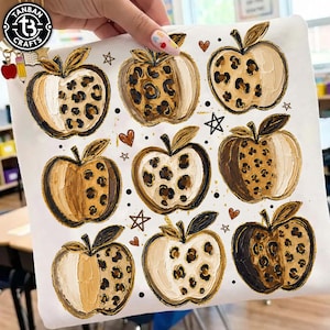 May include: A white fabric surface featuring a repeating pattern of nine apples. Each apple is rendered in shades of brown, cream, and tan with a textured paint effect. Some sections of the apples display a brown and black leopard print pattern.