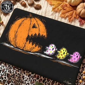 May include: A black rectangular surface featuring a graphic of a large orange jack-o'-lantern chasing three small ghosts. The ghosts are white with pink dots, yellow with orange pumpkins, and pink with flowers. The logo TANBAN CRAFTS is in the corner.