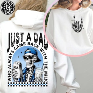 Pode incluir: Camisola branca com um gráfico de esqueleto usando óculos de sol e boné azul, segurando uma caixa de leite e um copo de leite. O texto diz "JUST A DAD WHO ALWAYS CAME BACK WITH THE MILK". Uma segunda camisola tem um gráfico de mão de esqueleto.