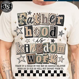 May include: Cream-colored t-shirt with the text "Fatherhood is Kingdom Work" in a mix of fonts and patterns. The shirt also features the quote "Train up a child in the way he should go; even when he is old he will not depart from it."