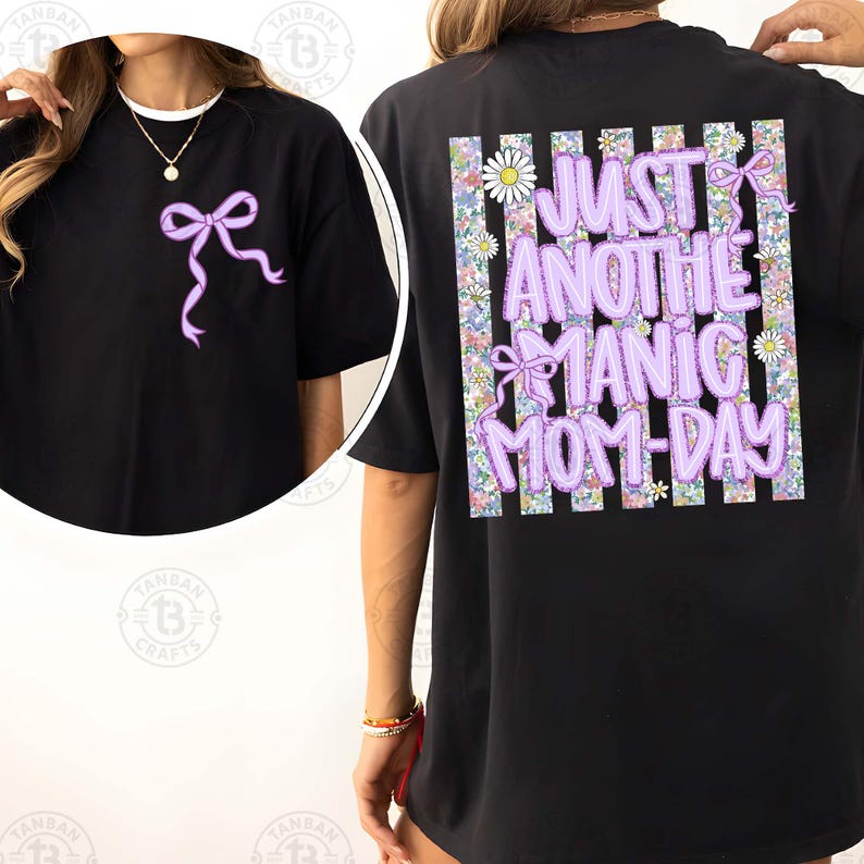 May include: Black t-shirt featuring a lavender bow on the front and the text "JUST ANOTHER MANIC MOM-DAY" on the back. The text is in lavender with a floral and daisy design.