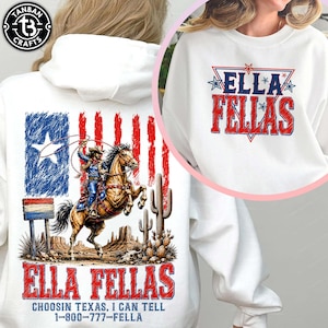 Puede incluir: Una sudadera con capucha blanca con un gráfico de un vaquero sobre un caballo encabritado en un paisaje desértico con una bandera de Texas. El texto dice ELLA FELLAS, CHOOSIN TEXAS, I CAN TELL y 1-800-777-FELLA. Un recuadro circular muestra el logo ELLA FELLAS.