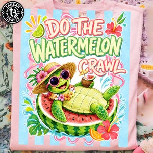 May include: Pink t-shirt with a colorful graphic of a turtle wearing sunglasses and a straw hat, lounging on a watermelon slice. Text reads "Do the Watermelon Crawl" in green and pink.