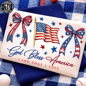 May include: A patriotic design featuring an American flag, red and blue bows, and stars. The text "God Bless America, Land That I Love" is displayed in blue and red script. The design is on a white background.
