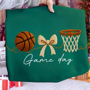 May include: A green fabric with a basketball, bow, and basketball net design. The words "Game day" are written in white script. The basketball is brown and the net is beige.