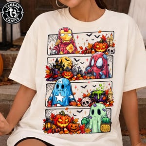 May include: A cream-colored t-shirt featuring a graphic print divided into four horizontal panels. The design displays various characters dressed as ghosts for Halloween, surrounded by pumpkins, bats, spiderwebs, a cauldron, and skulls.
