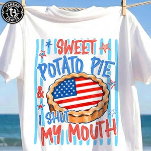 May include: White t-shirt with a graphic of a sweet potato pie featuring the American flag. The text reads "SWEET POTATO PIE & I SHUT MY MOUTH" in red and blue. The shirt is hanging on a clothesline.