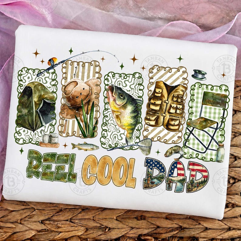 Op de afbeelding: Wit T-shirt met een visserij-thema ontwerp. Het ontwerp bevat illustraties van een tent, hengel, tacklebox, vissen en de tekst "Reel Cool Dad" met een Amerikaans vlagmotief. Het ontwerp is omlijst met groene en bruine decoratieve randen.