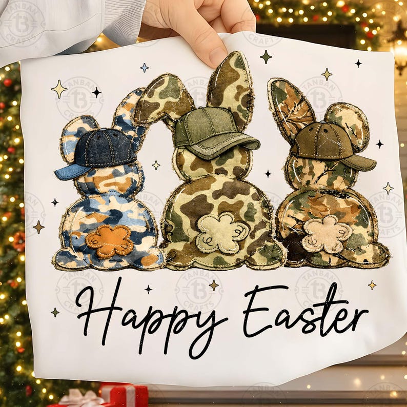 Op de afbeelding: Een wit Paaskussen met drie konijnenfiguren in camouflagepatronen, elk met een pet. De woorden "Happy Easter" staan in zwart schrift eronder. Decoratieve sterren omringen de konijnen.