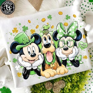 Puede incluir: Sudadera blanca con Mickey Mouse, Pluto y Minnie Mouse vestidos para el Día de San Patricio. Mickey lleva un sombrero verde, Pluto tiene un collar verde y Minnie un lazo verde y gafas. El diseño incluye tréboles y monedas.