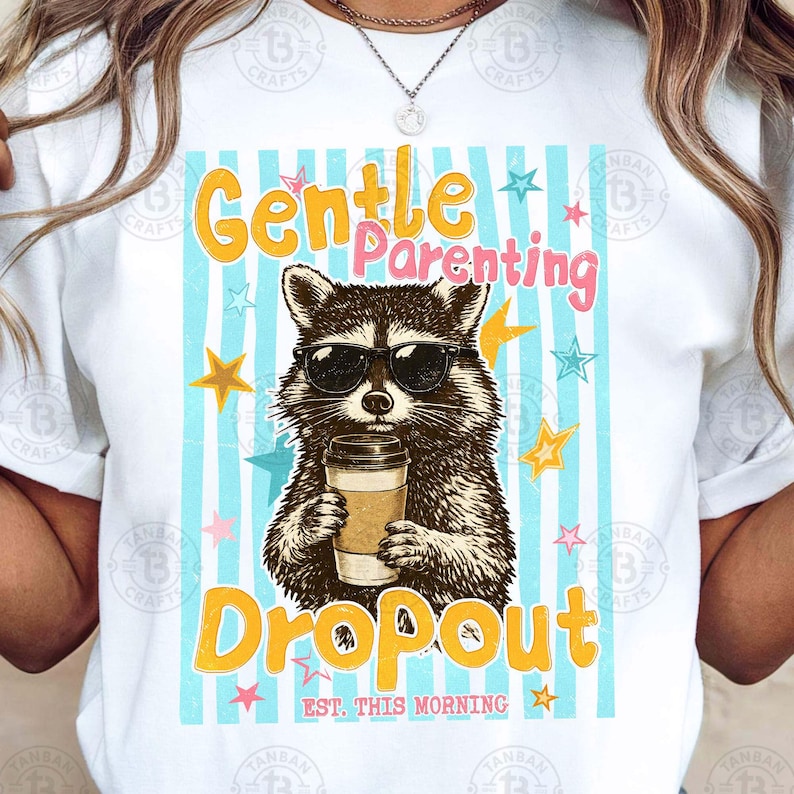 May include: White t-shirt with a raccoon wearing sunglasses, holding a coffee cup. The shirt features the text "Gentle Parenting Dropout" in yellow and pink, with stars and blue stripes.