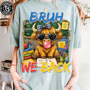 May include: A light blue t-shirt featuring a graphic of a fluffy highland cow wearing a blue plaid bow and heart-shaped sunglasses while blowing a pink bubble. The text reads BRUH WE BACK, with school supplies like books, a backpack, and a chalkboard.