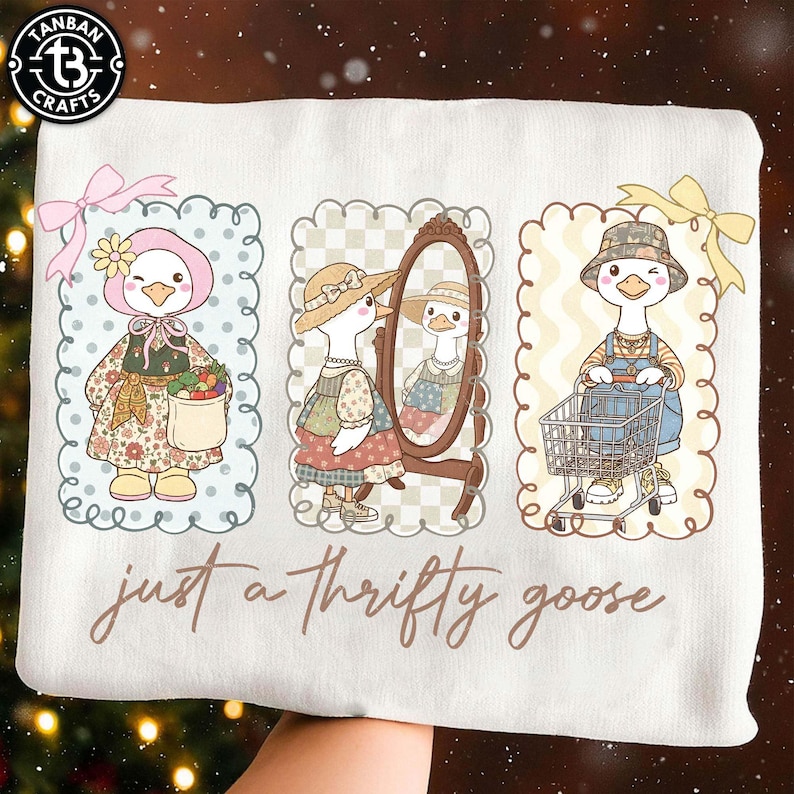 Puede incluir: Sudadera blanca con tres ilustraciones de gansos de dibujos animados. Los gansos est&aacute;n vestidos con varios atuendos, incluyendo un gorro, un vestido y un peto. El texto "just a thrifty goose" est&aacute; escrito en cursiva.
