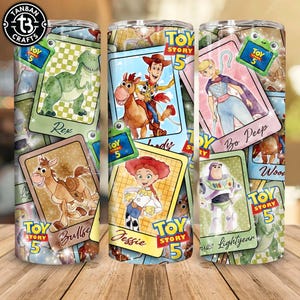 Peut inclure: Un gobelet cylindrique orné d'un motif de cartes à collectionner Toy Story 5. Les cartes présentent des personnages tels que Rex, Woody sur Bullseye, Bo Peep, Jessie et Buzz Lightyear, chacun étiqueté avec son nom et le logo Toy Story 5.