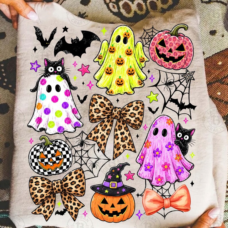 May include: A beige sweatshirt featuring a colorful Halloween-themed graphic print. The design includes ghosts, jack-o'-lanterns, black cats, leopard print bows, spider webs, bats, and stars in shades of pink, yellow, orange, and black.
