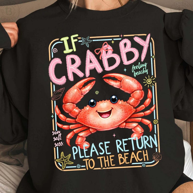 Może przedstawiać: Czarna bluza z kolorową grafiką uśmiechniętego kraba. Tekst brzmi "If Crabby, Please Return to the Beach." Projekt zawiera ilustracje słońca, rozgwiazd i muszli, ze słowami "sun, salt, sass" i "feeling beachy".
