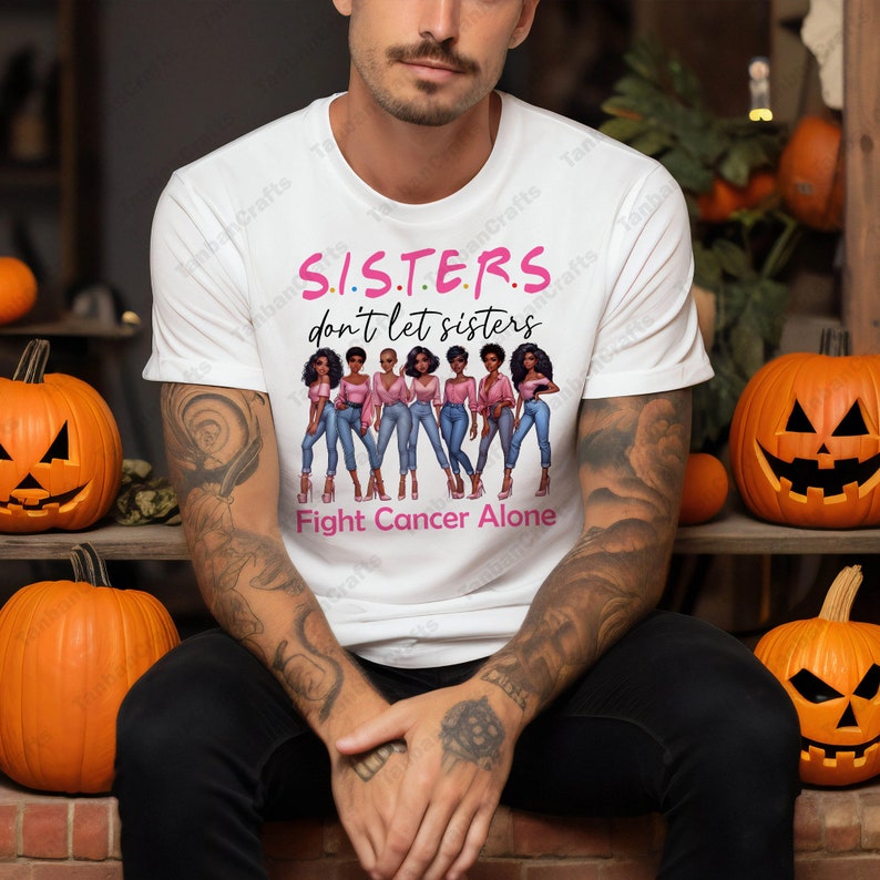 May include: White t-shirt with the text "S.I.S.T.E.R.S. don't let sisters Fight Cancer Alone." The shirt features a graphic of seven women in pink tops and blue jeans. Pumpkins with carved faces are in the background.