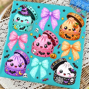 May include: A bright turquoise fabric featuring a repeating pattern of glittery, cartoon-style dumplings in open containers, interspersed with colorful bows, small stars, bats, skulls, and jack-o'-lanterns in shades of purple, orange, and white.