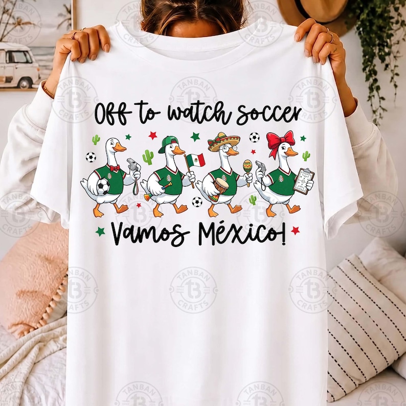 Pu&ograve; includere: Una t-shirt bianca con il testo "Off to watch soccer" e "VAMOS M&Eacute;XICO!" sopra e sotto un grafico di quattro anatre a cartoni animati che indossano maglie verdi, un fischietto, un berretto, un sombrero e un fiocco rosso per capelli.
