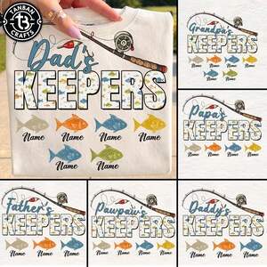 May include: A cream-colored t-shirt featuring a graphic of a fishing rod and the text "Dad's KEEPERS" in large block letters filled with small fish patterns. Below the text are six colorful fish illustrations, each with a "Name" label underneath.