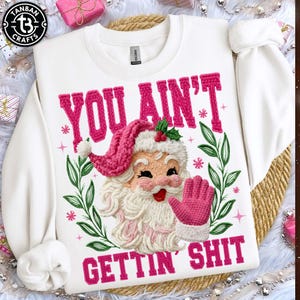 May include: White sweatshirt with a pink Santa Claus design and the text "YOU AIN'T GETTIN' SHIT". The Santa Claus has a pink hat and glove, with a white beard and a smiling face. The design includes green leaves and pink snowflakes.
