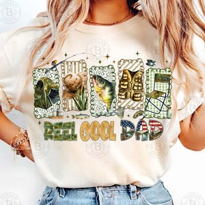 Op de afbeelding: Cr&egrave;mekleurige sweatshirt met een visserij-thema grafiek. Het ontwerp bevat visgerei, een vis en de tekst "REEL COOL DAD" in een mix van kleuren en lettertypen. De afbeelding is omlijst met een decoratieve rand.