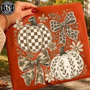 May include: A burnt orange fabric featuring a graphic print of two pumpkins, one with a white and brown checkered pattern and one with a white leaf design, accompanied by a leopard print bow, a camouflage bow, and several small white flowers.