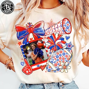 Könnte beinhalten: Cremefarbenes T-Shirt mit einem patriotischen Design mit Football, Megaphon und Schleife. Das Design enthält das Wort "CHEER", ein Foto, Sterne und Herzen in Rot, Weiß und Blau. Das Shirt hat auch den Text "#1".