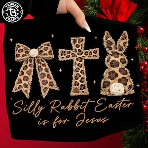 May include: Black t-shirt featuring a bow, cross, and bunny, all with a leopard print design. The bow and bunny have white accents. The text "Silly Rabbit Easter is for Jesus" is written in cursive.