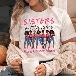 May include: White t-shirt with the text "S.I.S.T.E.R.S don't let sisters Fight Cancer Alone". The shirt features a graphic of seven women in pink tops and blue jeans.
