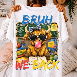May include: A white t-shirt featuring a graphic of a fluffy Highland cow wearing a blue plaid bow and heart-shaped sunglasses while blowing a pink bubble. The cow sits before a chalkboard with the text BRUH WE BACK and school supplies.